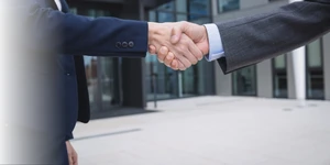 Dos personas dándose la mano frente a un edificio corporativo
