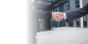 Dos personas dándose la mano frente a un edificio corporativo